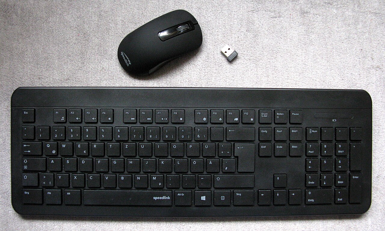 밝은 천 위에 놓인 검은색 무선 키보드와 마우스, 작은 USB 수신기