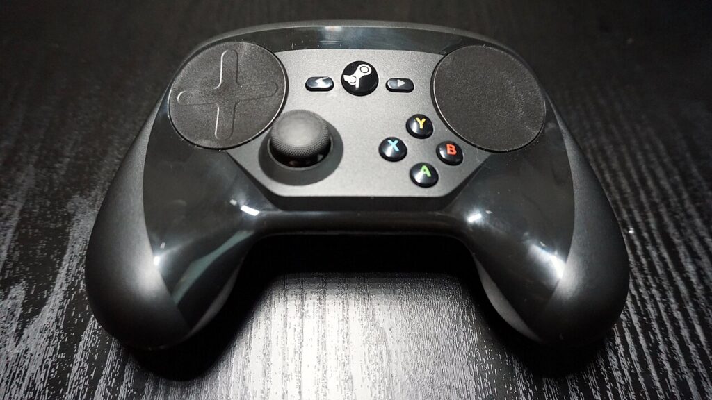 검은 테이블 위 Steam Controller(2015)의 앞면. 두 원형 트랙패드와 왼쪽 스틱, 오른쪽 A·B·X·Y 버튼이 보인다.