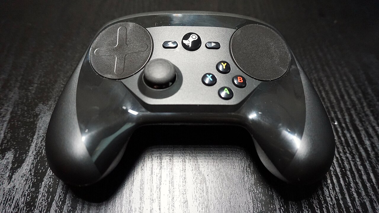 검은 테이블 위 Steam Controller(2015)의 앞면. 두 원형 트랙패드와 왼쪽 스틱, 오른쪽 A·B·X·Y 버튼이 보인다.